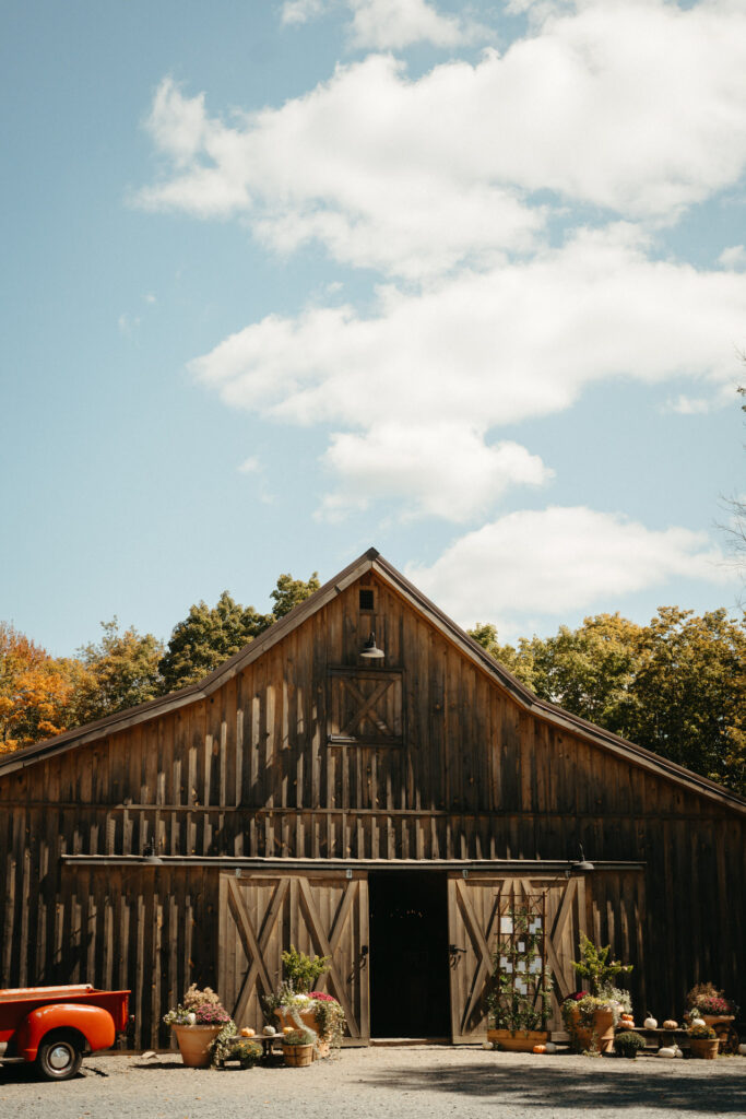 Weathered barn with open doors, flower pots and a red truck out front