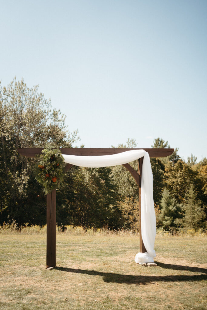 Wooden ceremony arch draped with white fabric and greenery