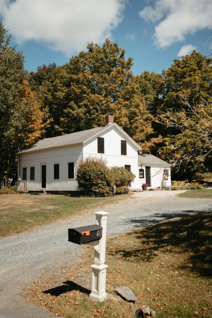 White farmhouse beside a gravel drive and a mailbox