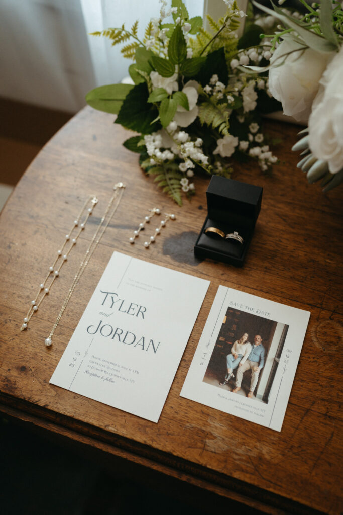 Rings in a box, jewelry and an invitation reading Tyler and Jordan on a wooden table