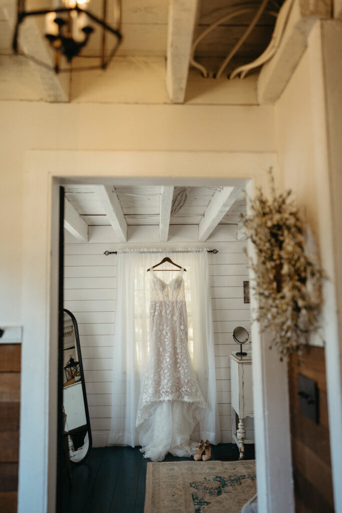 Wedding gown hanging in a white-paneled room, seen through a doorway