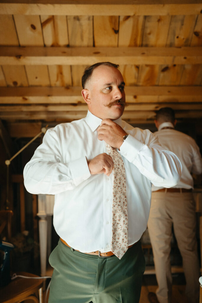 Person in a white shirt adjusting their tie in a wood-beamed room