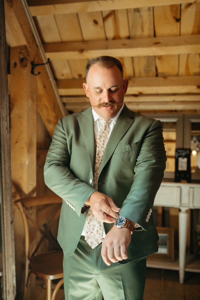 Person in a green suit fixing their cuff in a wood-beamed room