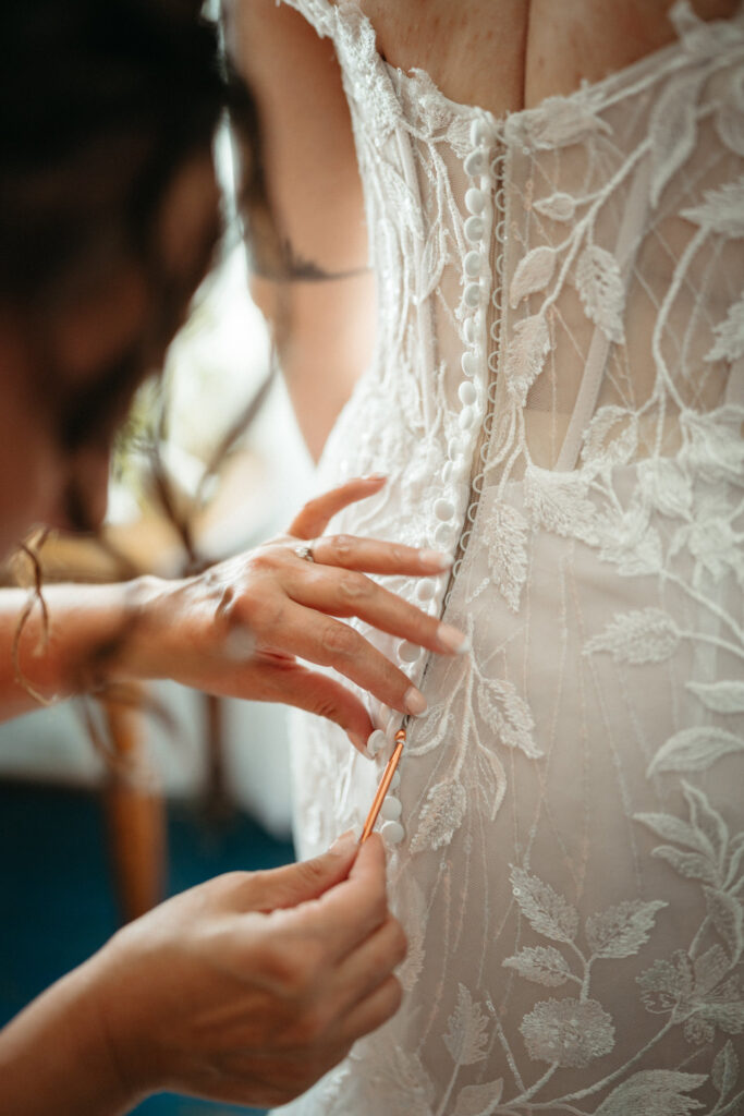 Hands fastening the buttons on the back of a lace gown