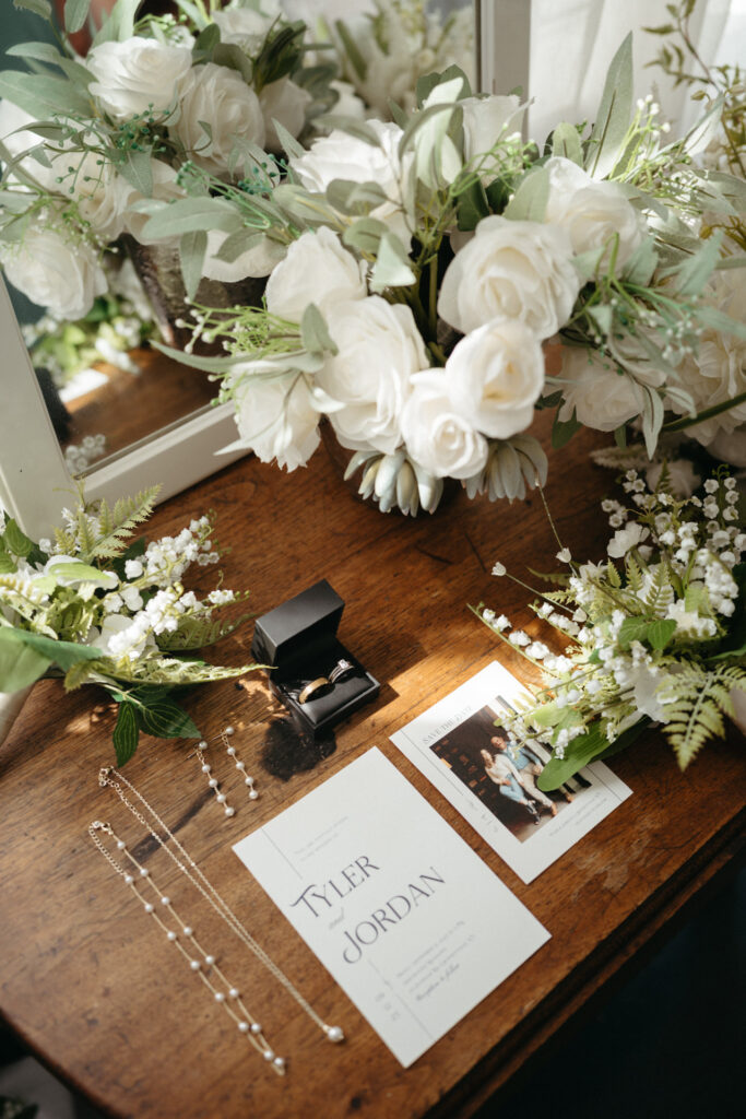 White flower bouquet, rings, jewelry and an invitation on a wooden table