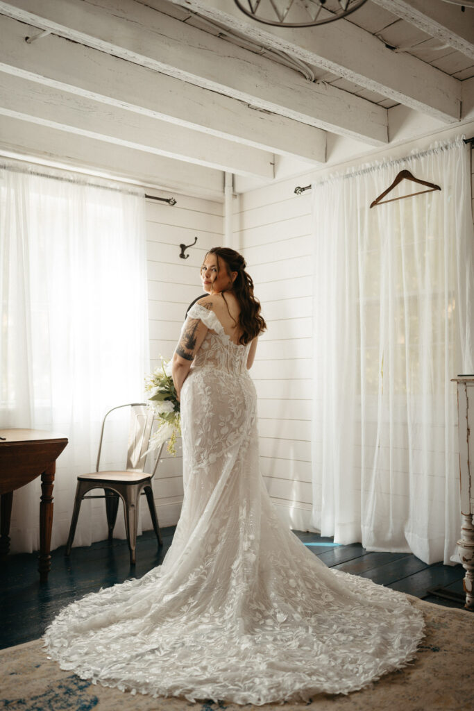 Person in a lace gown with a long train facing a sunlit window