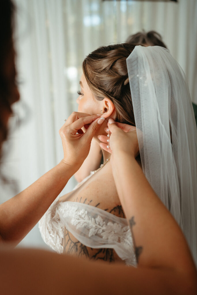 Close-up of a person in a veil putting on an earring with a helping hand