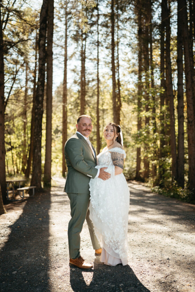 Couple standing close and smiling on a gravel path among tall trees