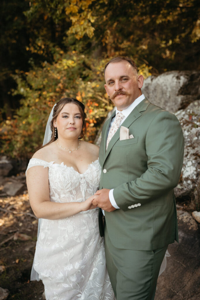 Couple in a green suit and lace gown holding hands beside boulders