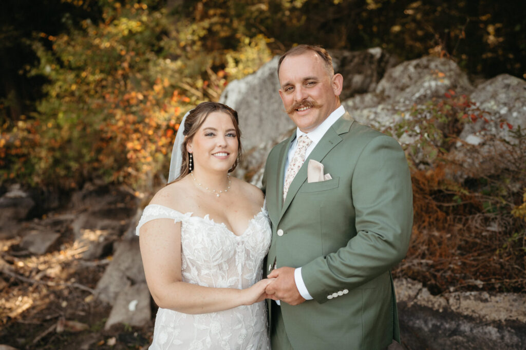 Couple smiling with joined hands beside boulders and autumn leaves