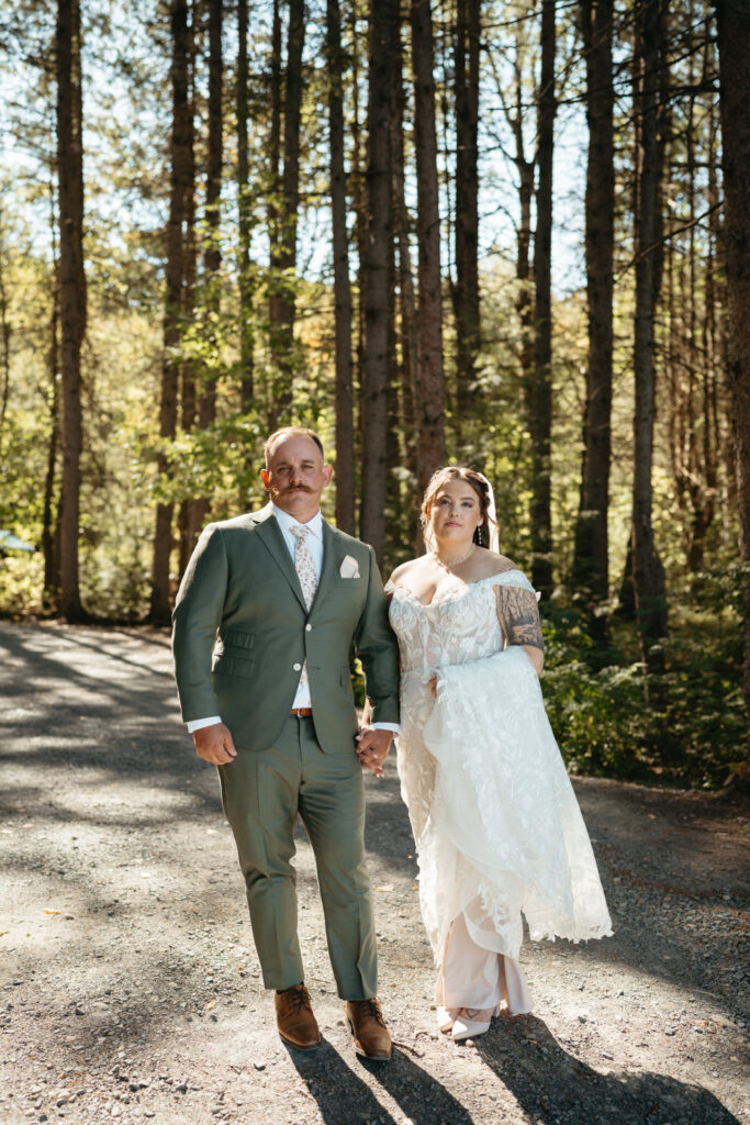 Couple in a green suit and lace gown standing hand in hand on a path