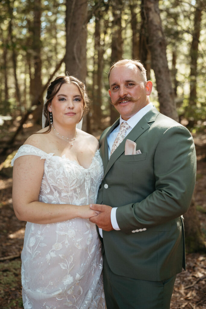 Couple smiling at the camera, holding hands, among tall trees
