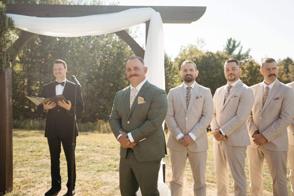 Officiant and wedding party in beige suits waiting under a draped arch