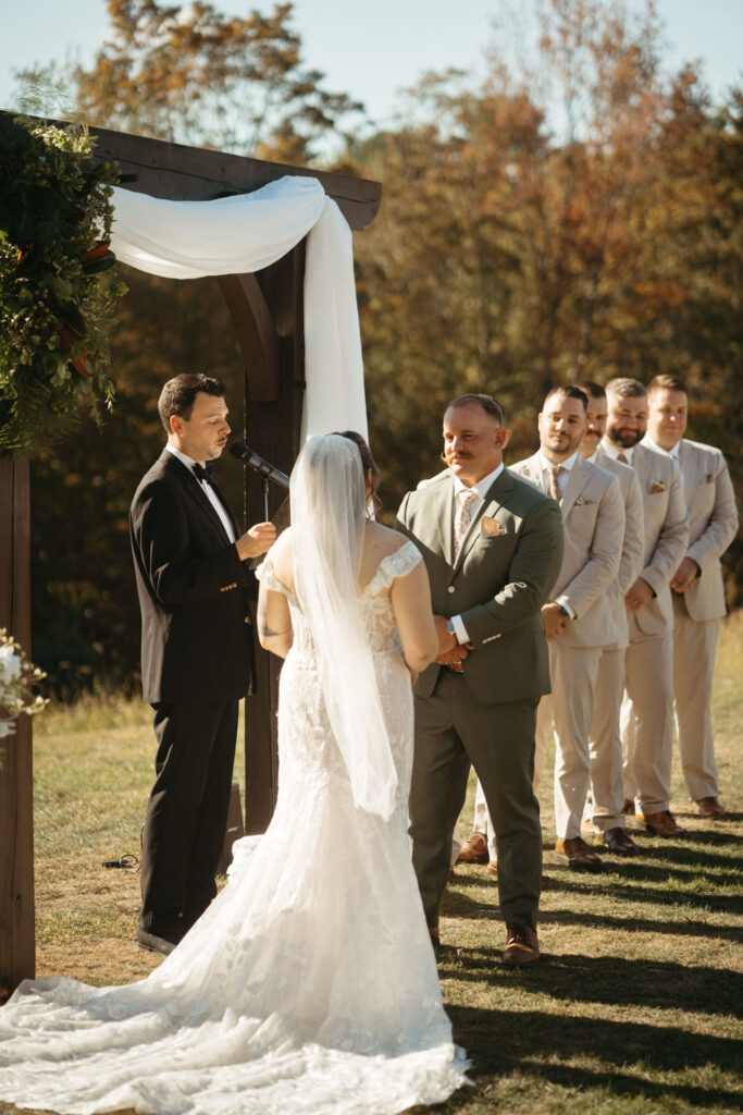 Person in a veil facing their partner and the officiant under the arch, long train behind them