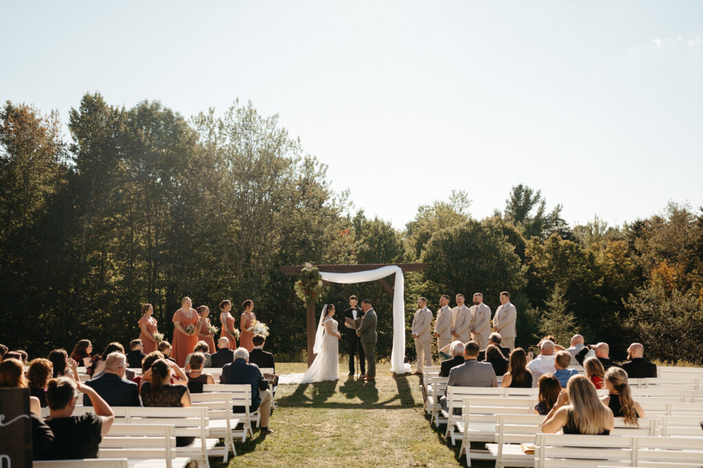 Wide view of an outdoor ceremony with guests on white benches
