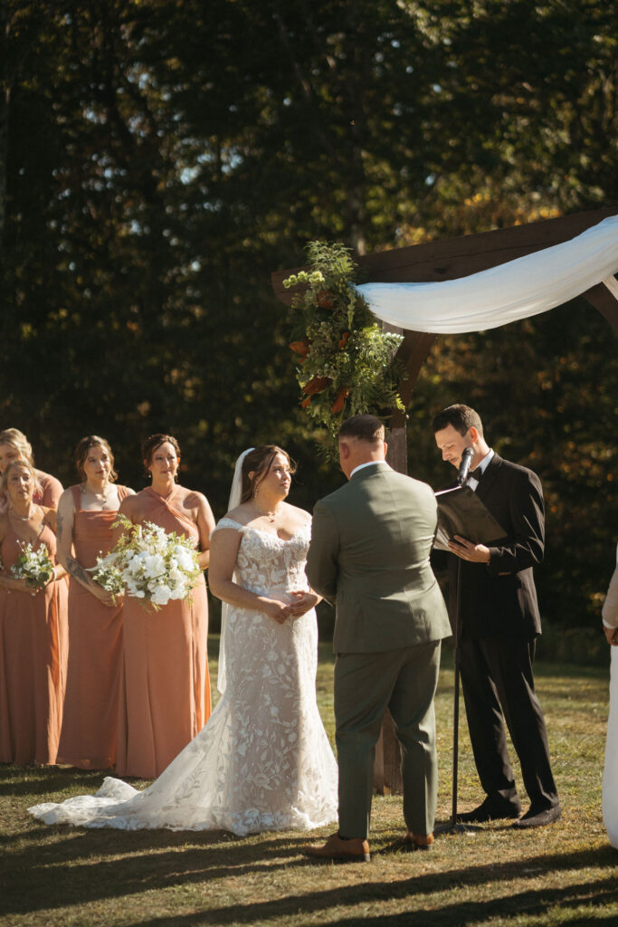 Couple at the arch with attendants in rust gowns and an officiant
