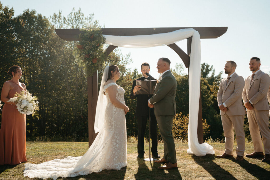 Couple and officiant under a draped arch, wedding party on both sides