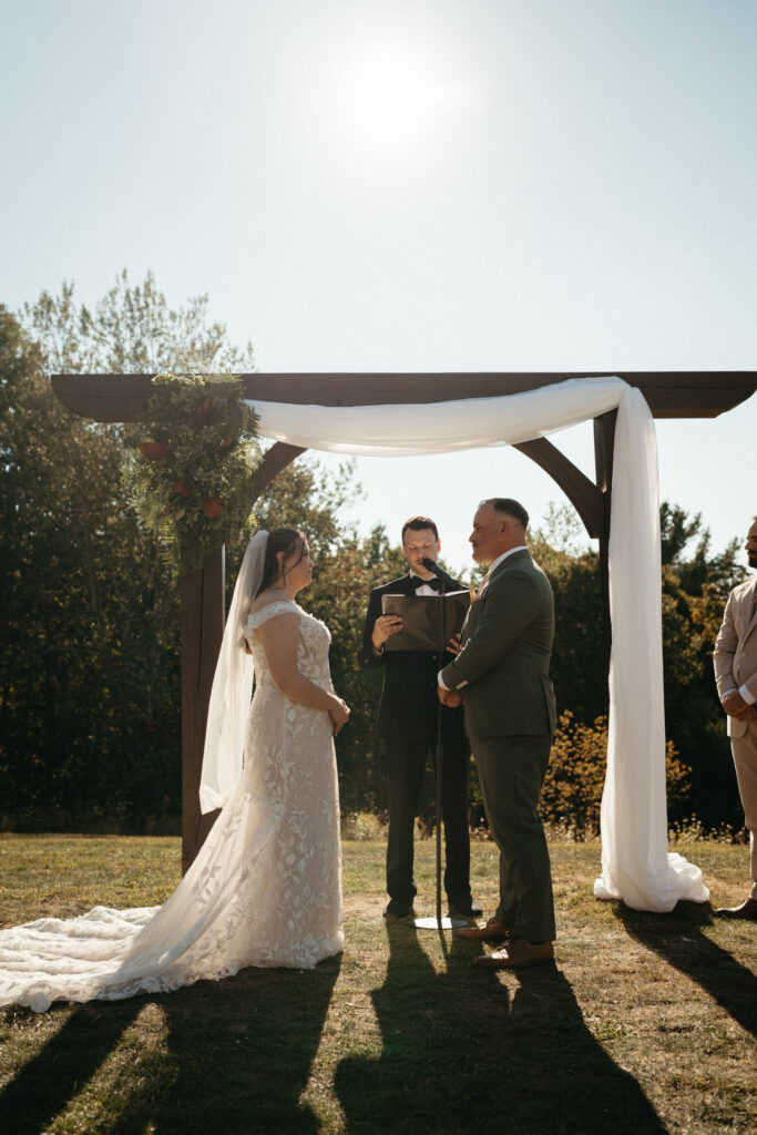 Couple exchanging vows under a draped wooden arch with the officiant between them