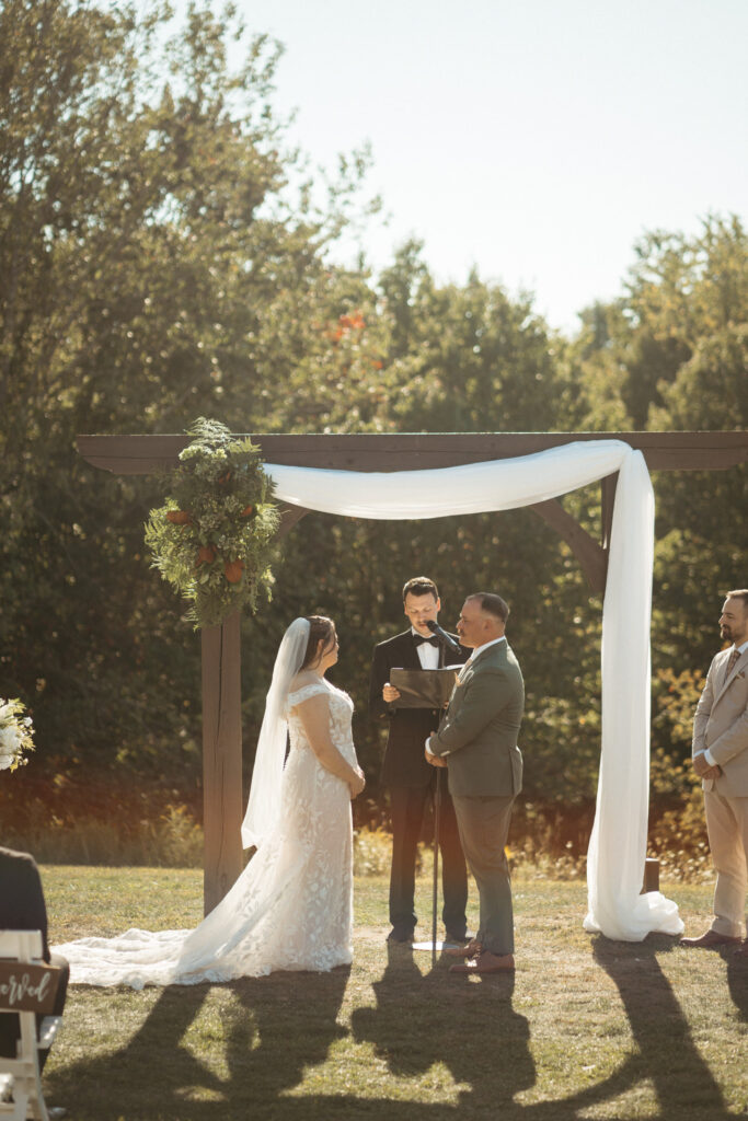 Couple at the arch with a long train spread across the grass