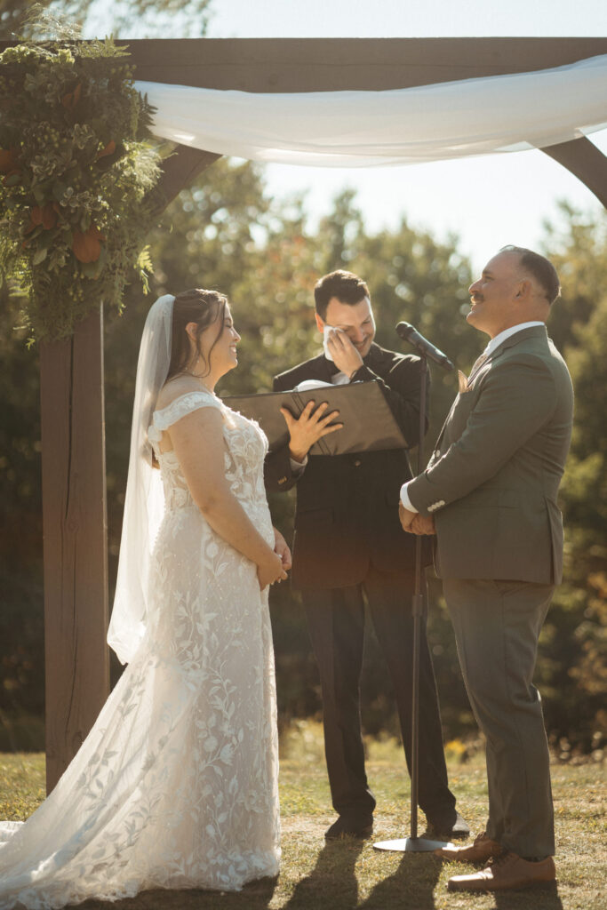 Officiant wiping a tear while the couple stands at the arch