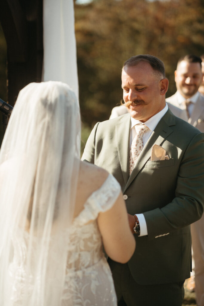 Person in a green suit smiling at a person in a veil during vows