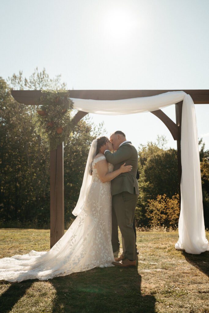 Couple kissing under the draped arch in bright sunlight