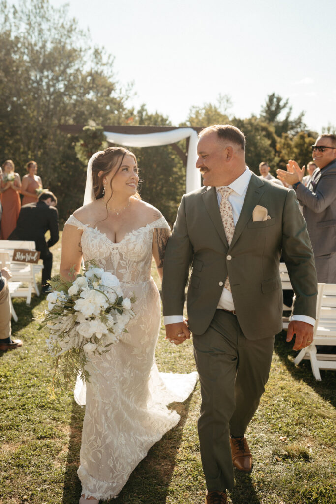 Couple walking back down the aisle holding hands as guests applaud