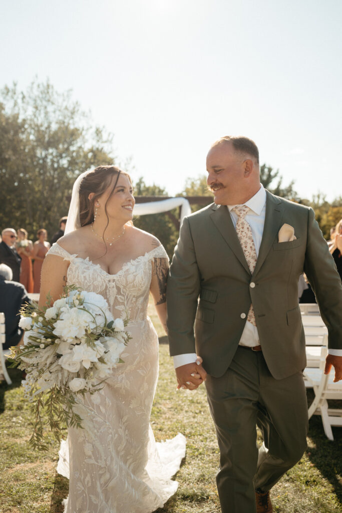 Couple holding hands and smiling at each other as they walk the aisle