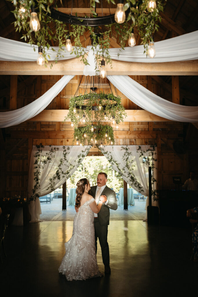 Couple's first dance in a barn under chandeliers and draped fabric