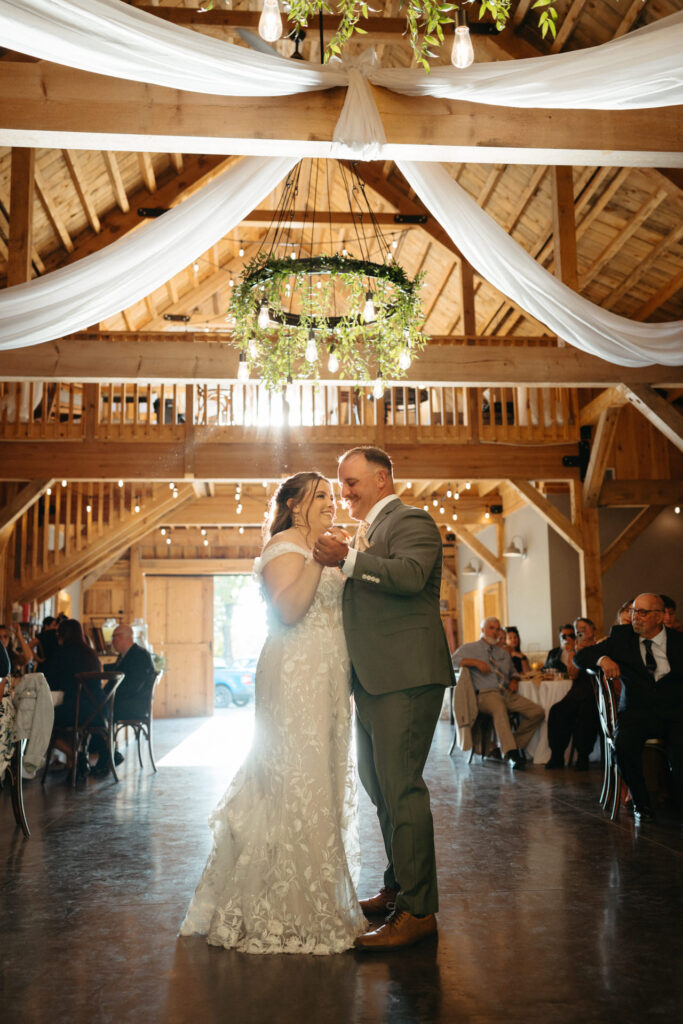 Couple sharing a dance in the barn as guests watch from their tables