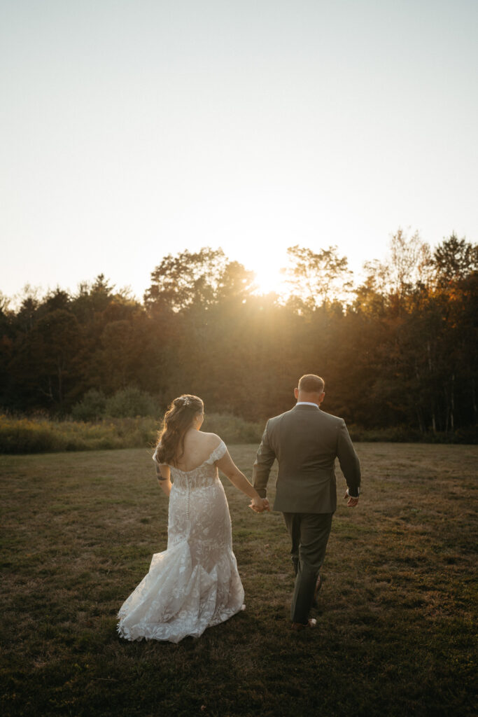 Couple walking hand in hand across a field at sunset, seen from behind