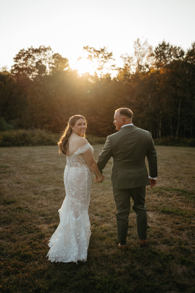 Couple walking across a field at sunset, one looking back over their shoulder