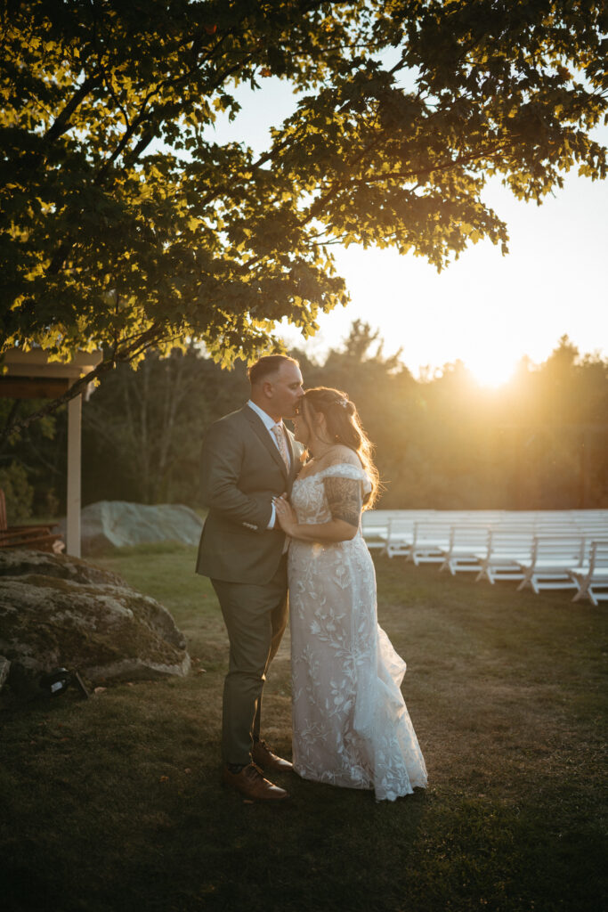 Couple embracing under a tree with white ceremony benches behind them