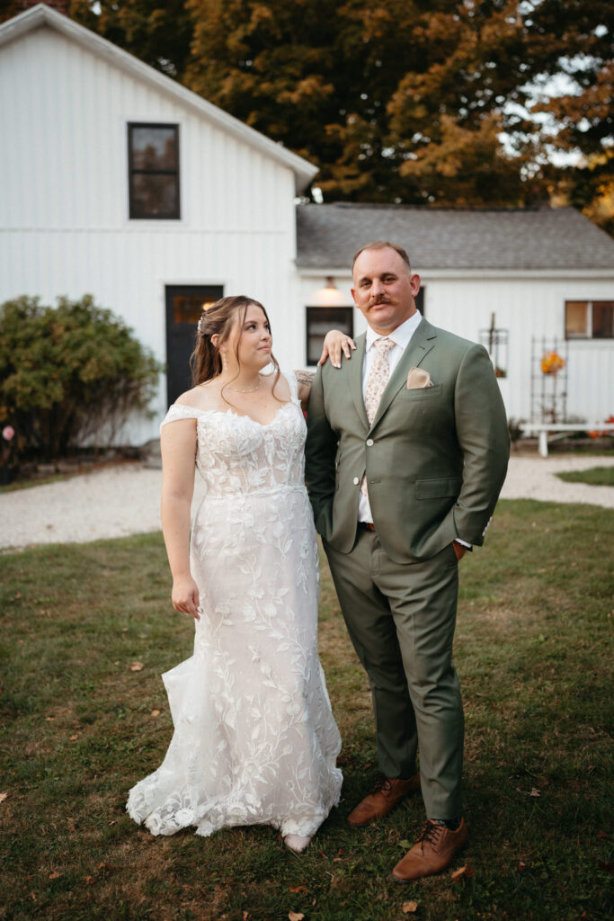 Couple standing together on a lawn in front of a white farmhouse