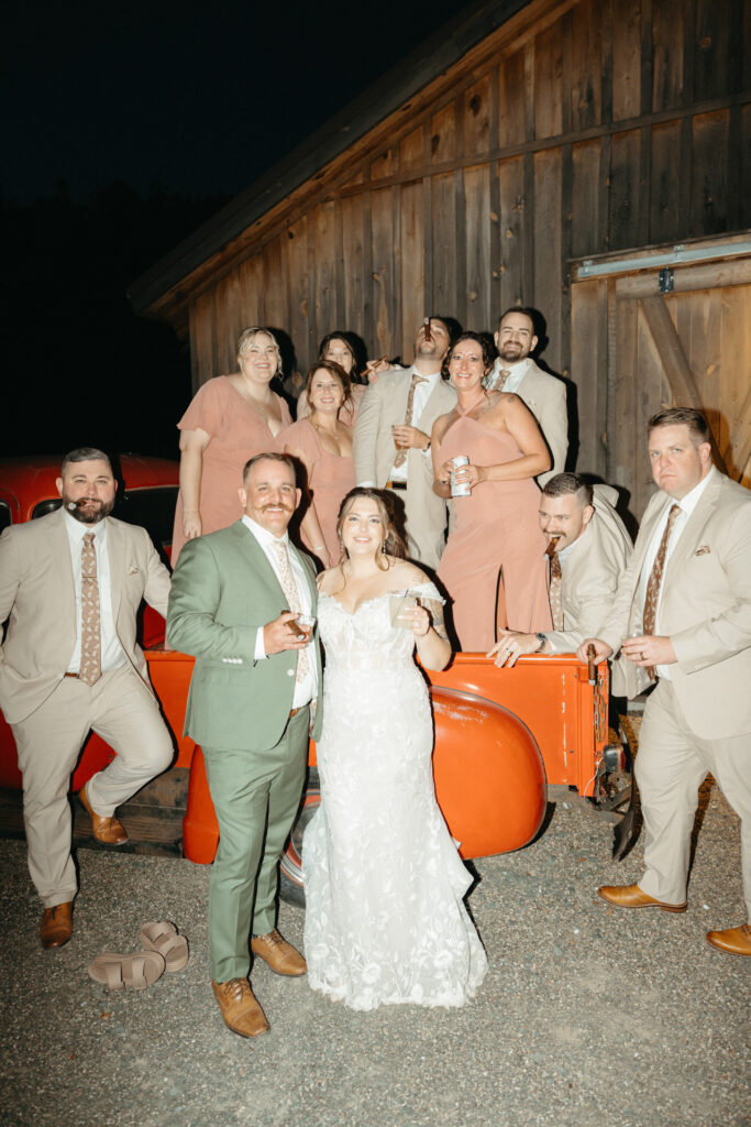 Wedding party posing together in front of a barn at night beside an orange truck