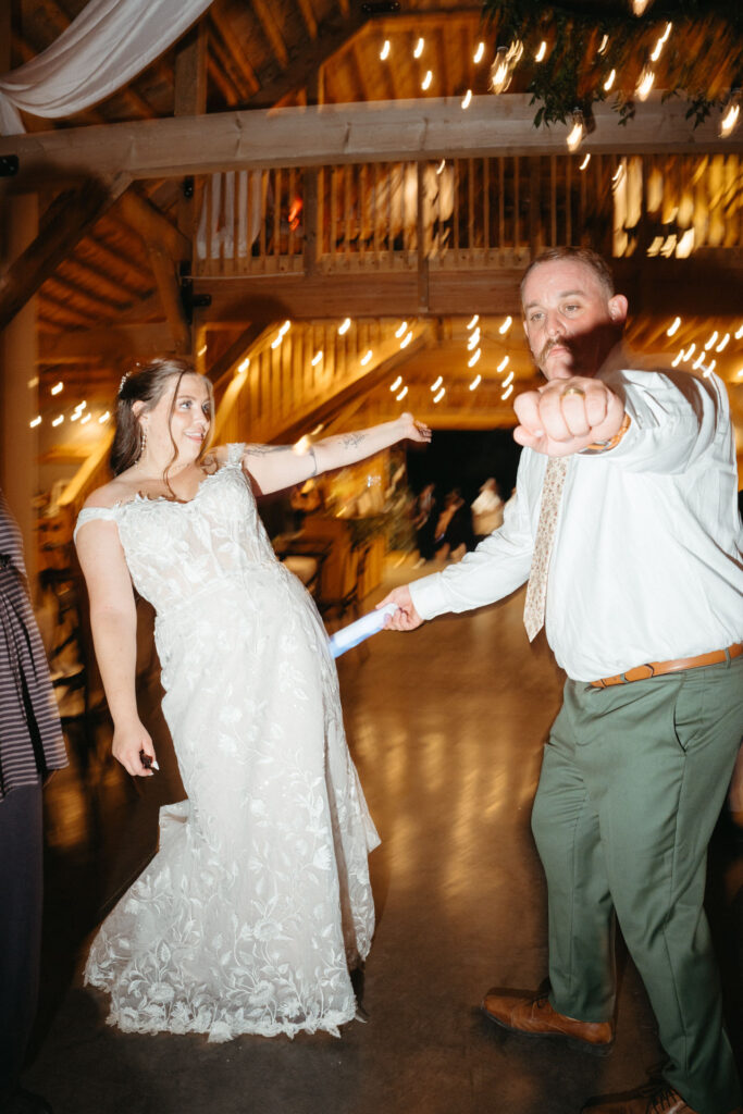Couple dancing at the reception with glow sticks, one pointing at the camera