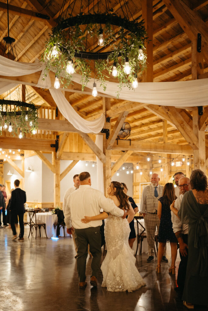 Couple slow dancing in the barn as guests mingle