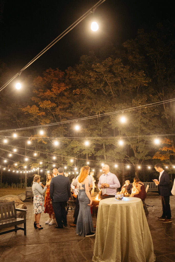 Guests mingling around the fire pit under string lights at night