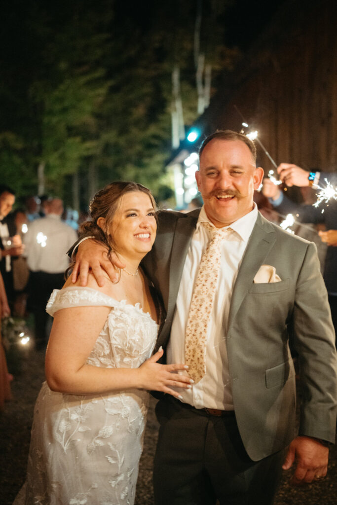 Couple smiling arm in arm at the sparkler send-off