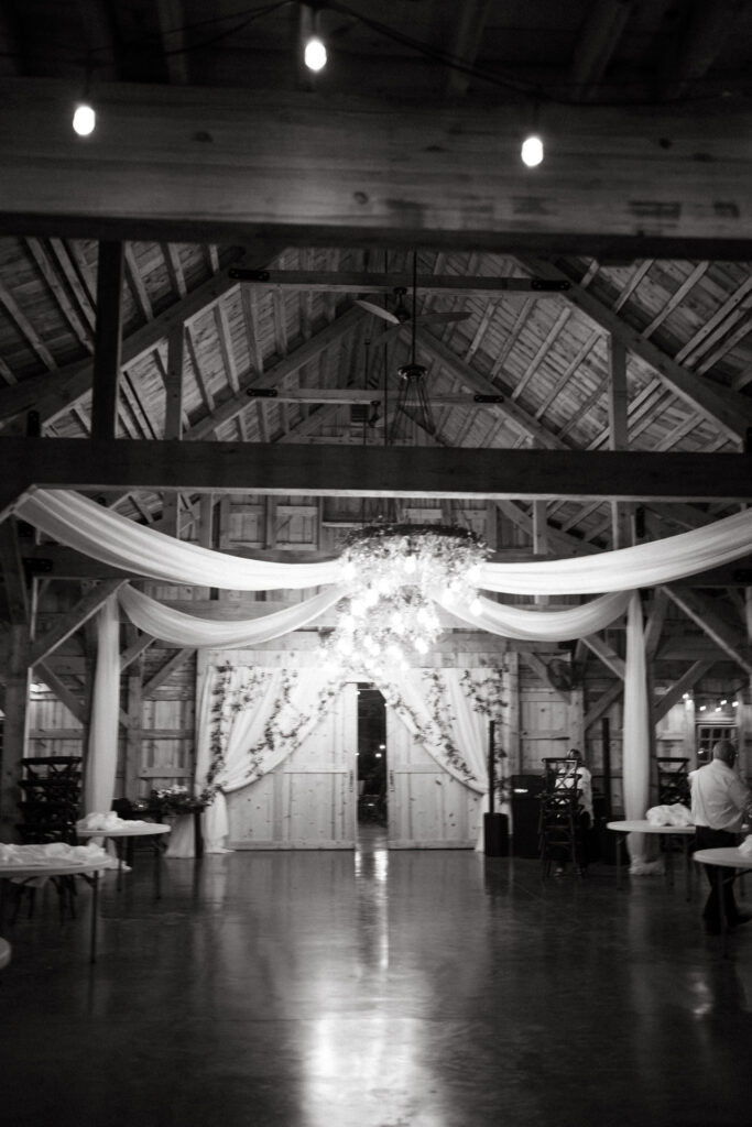 Black and white view of the empty barn hall with a chandelier and draped fabric