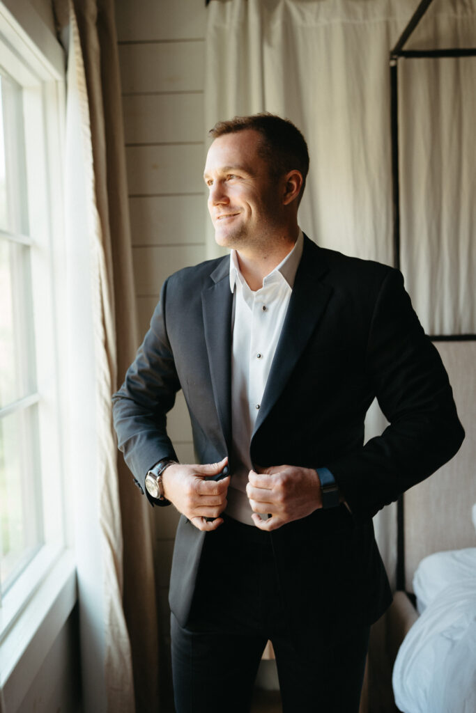 Person in a dark suit adjusting their jacket by a window