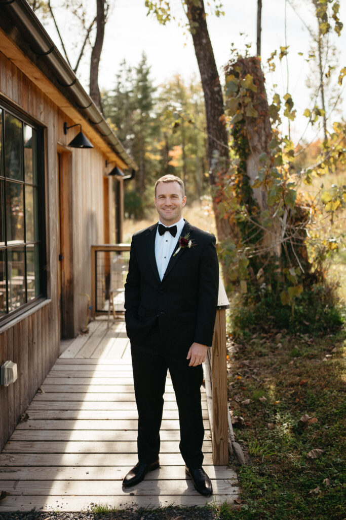 Person in a tuxedo standing on a wooden walkway beside a cabin