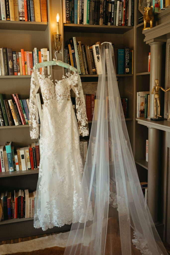 Wedding gown and veil hanging in front of a bookshelf