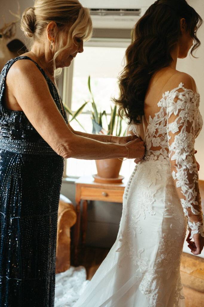 Person in a navy beaded dress helping button a lace gown