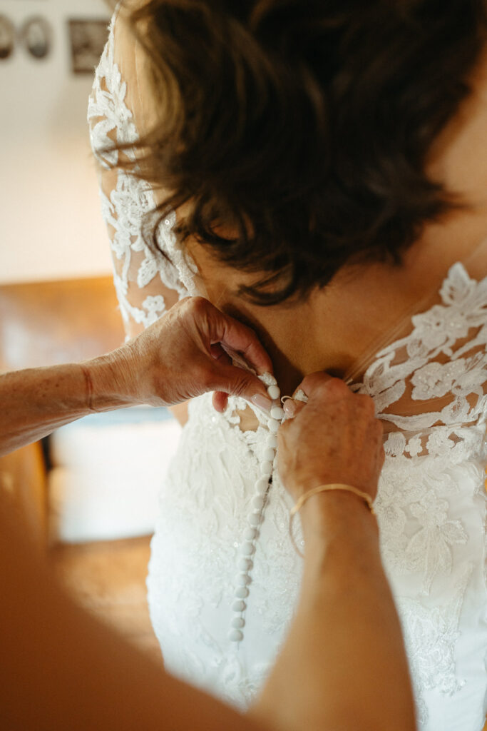 Hands fastening the buttons on the back of a lace gown