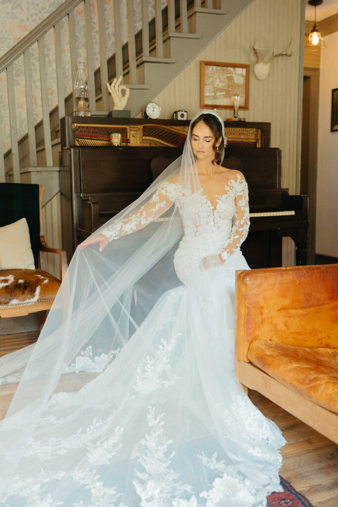 Person in a lace gown and veil seated by a piano near a staircase