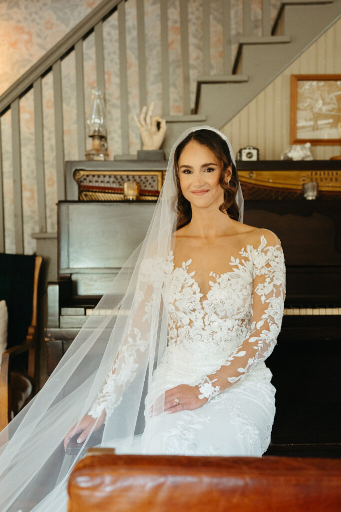 Person in a lace gown and veil smiling, seated by a piano