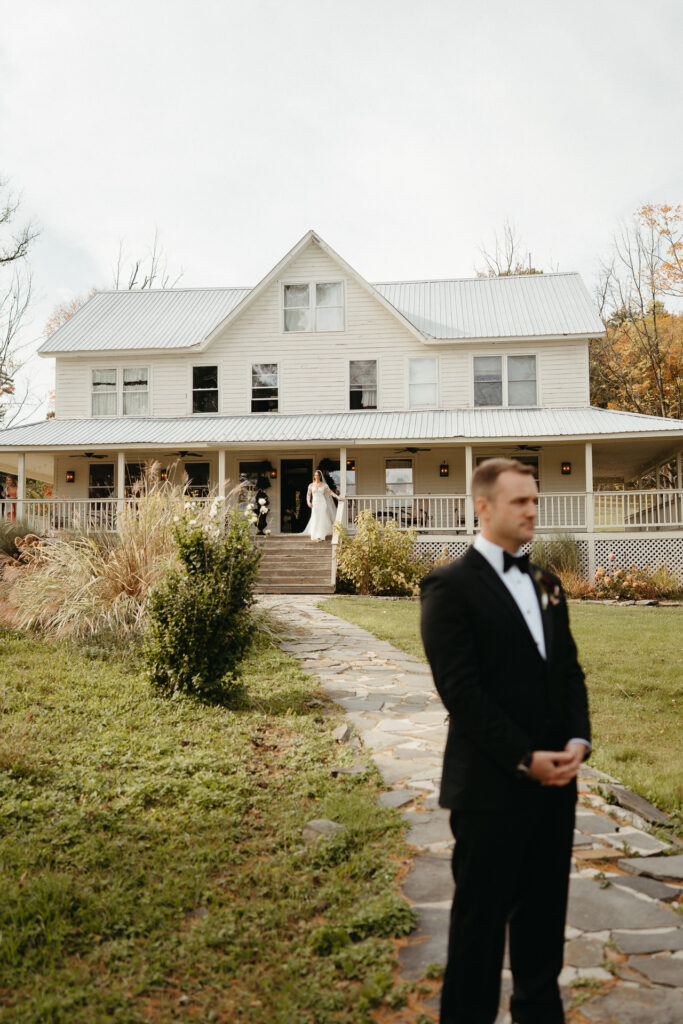 Person in a tuxedo waiting with their back turned in front of the farmhouse