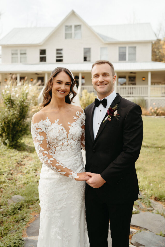 Couple smiling and holding hands in front of the farmhouse