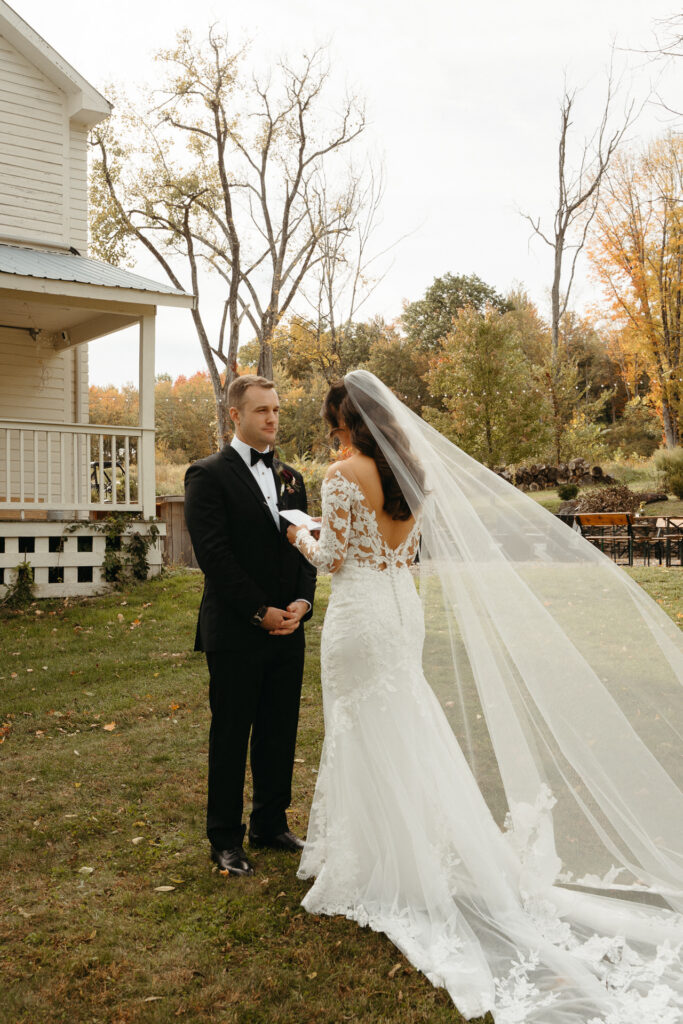 Couple reading notes in front of the farmhouse, a long veil trailing